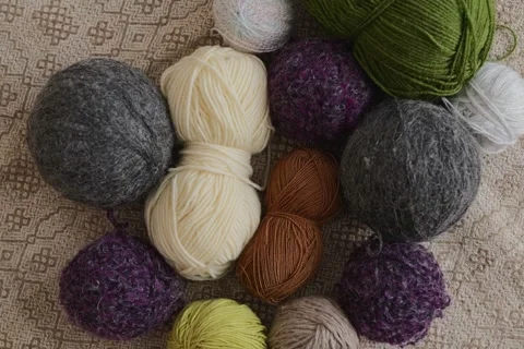 Different balls of yarn and wool are spread out on a light patterned surface. Vidéo 336464790