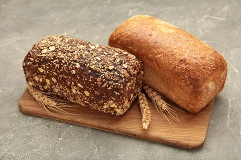 Different bread on cutting board on grey concrete background. Stock Photos