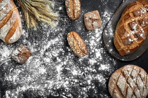 Different bread with flour and spikelets of wheaton black background Stock Photos