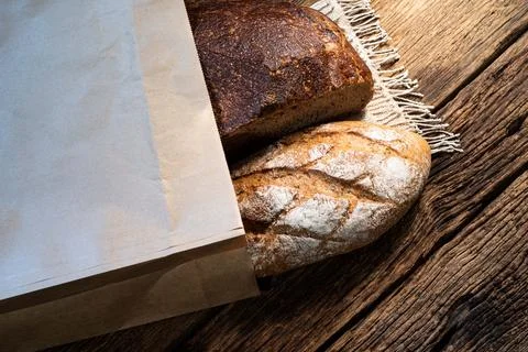 Different bread rye and baguette in bag isolated on wood background. Stock Photos