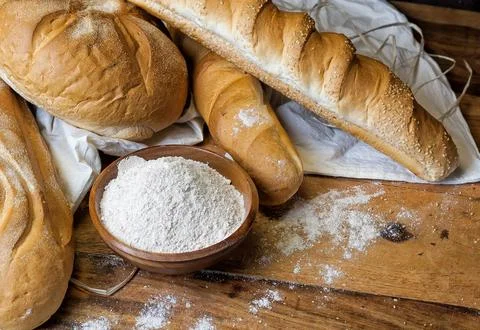 Different bread on the wooden table, flour, sackcloth, bowl Stock Photos