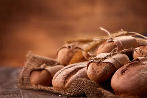 Different bread on the wooden table, paper bags, burlap, rope and ears of wheat Stock Photos
