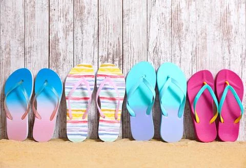 Different bright flip flops on sand near wooden wall, space for text. Summer  Stock-Fotos