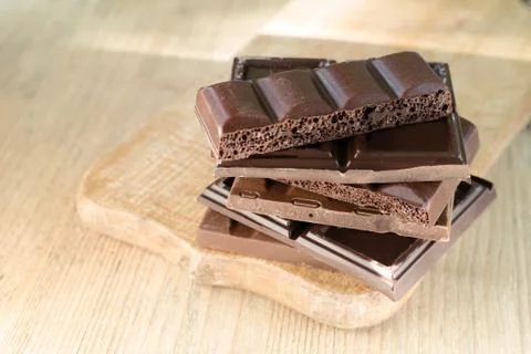 Different broken chocolate bars stacked on a wooden board. Stock Photos