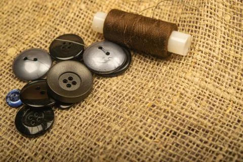 Different buttons and a spool of thread on the burlap with a rough texture. C Foto stock