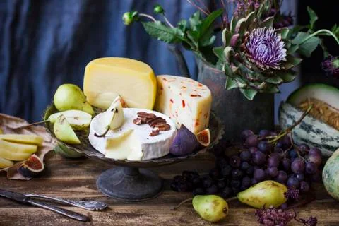The different cheese, fresh fruit and garden flowers on old wooden table and  Stock Photos