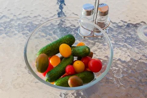 Different cherry tomatoes and cucumbers in bowl on glass table Foto stock