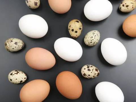 Different chicken eggs lie randomly on dark background Stock Photos