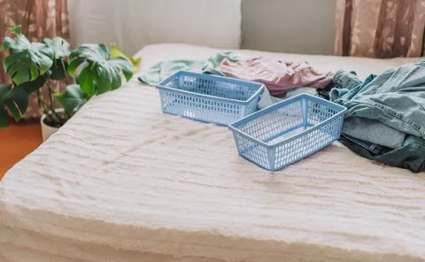 Different clothes with blue containers on a made bed Stock Photos