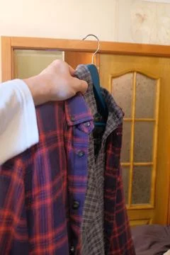 Different clothes in a persons hand on a hanger, shirts of different styles and Stock Photos