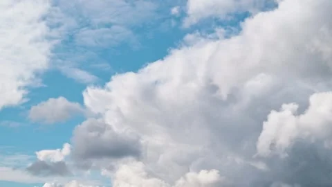 Different cloud shapes slowly transform in a clear blue sky, showcasing the Stock Footage 338299534