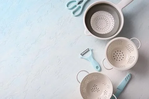 Different colanders with scissors, knife and vegetable peeler on light backgr Stock Photos