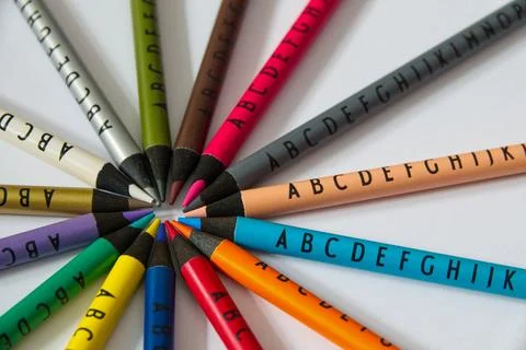 Different colored crayons with letters arranged in a circle on white background Stock Photos