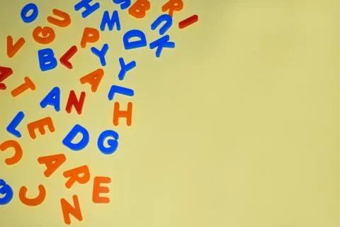 Different colored letter blocks scattered over a yellow paper background Stock Photos