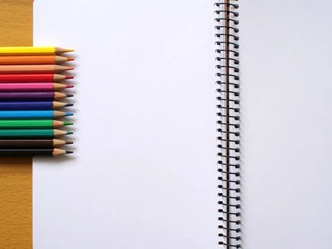 Different colored pencils next to note book with blank page Foto stock