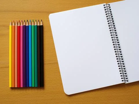 Different colored pencils next to note book with blank page Stock Photos