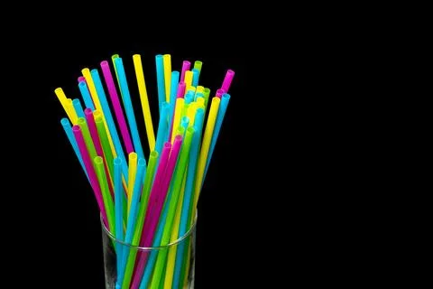 Different colored plastic drinking straws placed in a glass black background Stock Photos