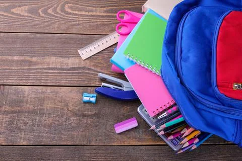 Different colored school accessories falling out of a school backpack on a br Stock Photos