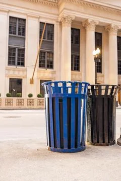 Different colored trash bins located on a city sidewalk in front of a large.. Stock Photos
