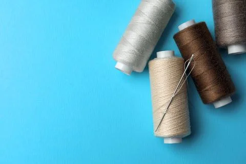 Different colorful sewing threads with needle on light blue background, fla.. Stock Photos