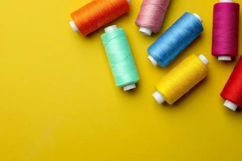 Different colorful sewing threads on yellow background, flat lay. Space for.. Stock Photos