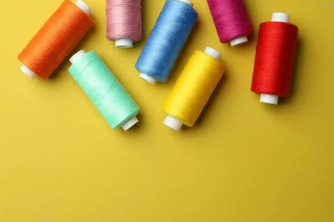 Different colorful sewing threads on yellow background, flat lay. Space for.. Stock Photos