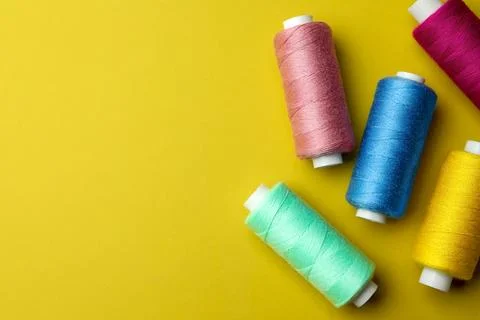 Different colorful sewing threads on yellow background, flat lay. Space for.. Stock Photos