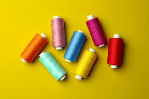 Different colorful sewing threads on yellow background, flat lay Stock Photos
