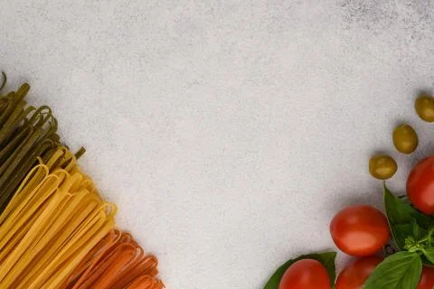 Different colour spaghetti and vegetables on a stone background. Stock Photos