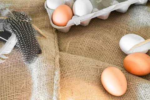 Different coloured eggs with feathers lying on a jute bag Foto stock