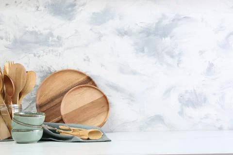Different dishware and utensils on white marble table against textured wall.  Stock Photos