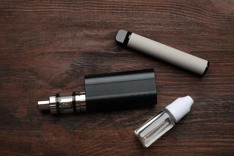 Different electronic cigarettes and vaping liquid on wooden table, flat lay.  Stock Photos