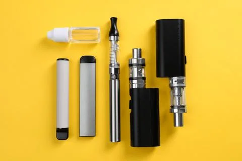 Different electronic cigarettes and vaping liquid on yellow background, flat  Stock Photos