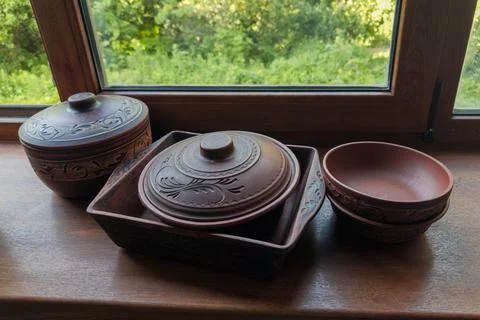 Different empty red clay crockery on wooden windowsill against window Stock Photos