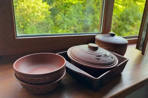 Different empty red clay crockery on wooden windowsill against window Stock Photos