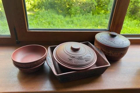 Different empty red clay crockery on wooden windowsill against window Stock Photos