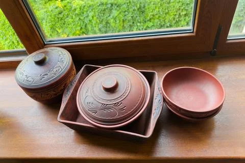 Different empty red clay crockery on wooden windowsill against window Stock Photos