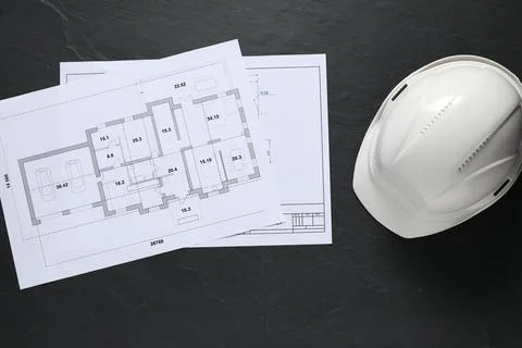 Different engineering drawings and hard hat on black table, flat lay. Space.. Stock Photos