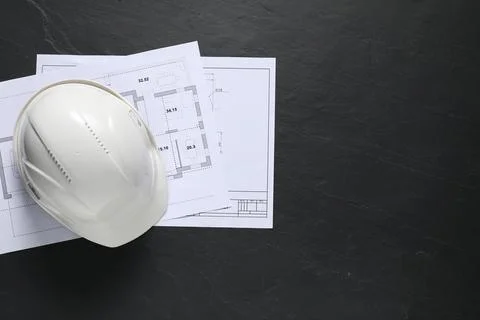 Different engineering drawings and hard hat on black table, flat lay. Space.. Stock Photos