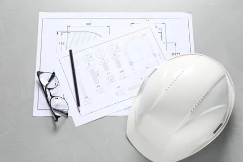 Different engineering drawings, hard hat, pencil and glasses on grey table,.. Stock Photos