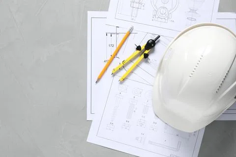 Different engineering drawings, hard hat, pencil and divider on grey table,.. Stock Photos