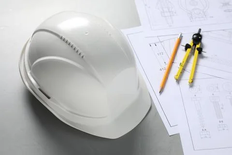 Different engineering drawings, hard hat, pencil and divider on grey table,.. Stock Photos