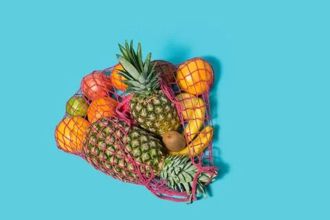 Different fruits lie in a string bag on a blue background. concept of shopping Stock Photos