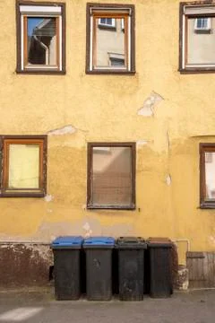 Different garbage cans in front of an old house whose plaster crumbles and cr Stock Photos