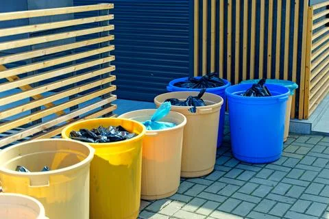 Different garbage cans with garbage bags stand near the wall Stock Photos