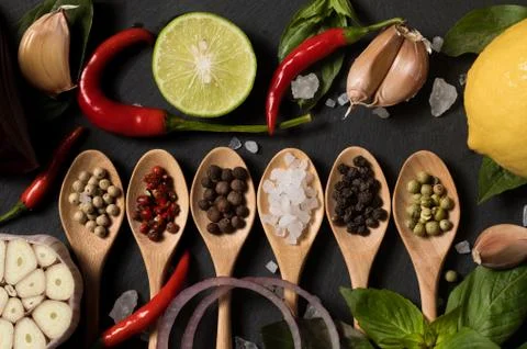 Different kind of pepper and salt with garlic in wooden spoons on a black sla Stock Photos