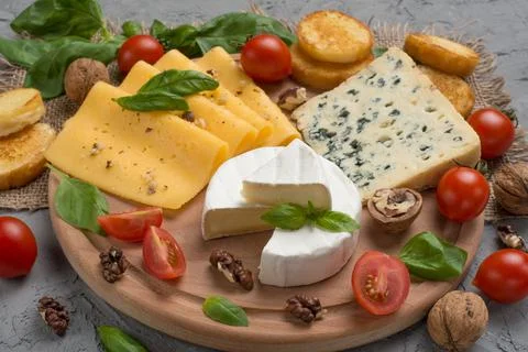 Different kinds of cheeses, with basil, cherry tomatoes, croutons from baguet Stock Photos