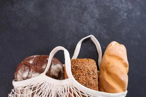 Different kinds of fresh bread in white mesh tote bag Stock Photos