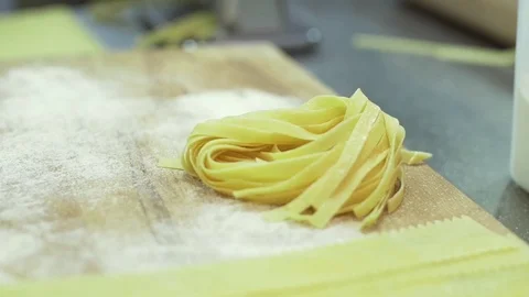 Different kinds of raw pasta lie on a wooden table in flour. Chef turns over a Stock Footage 74718350