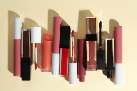 Different lip glosses and applicators on pale yellow background, flat lay Stock Photos